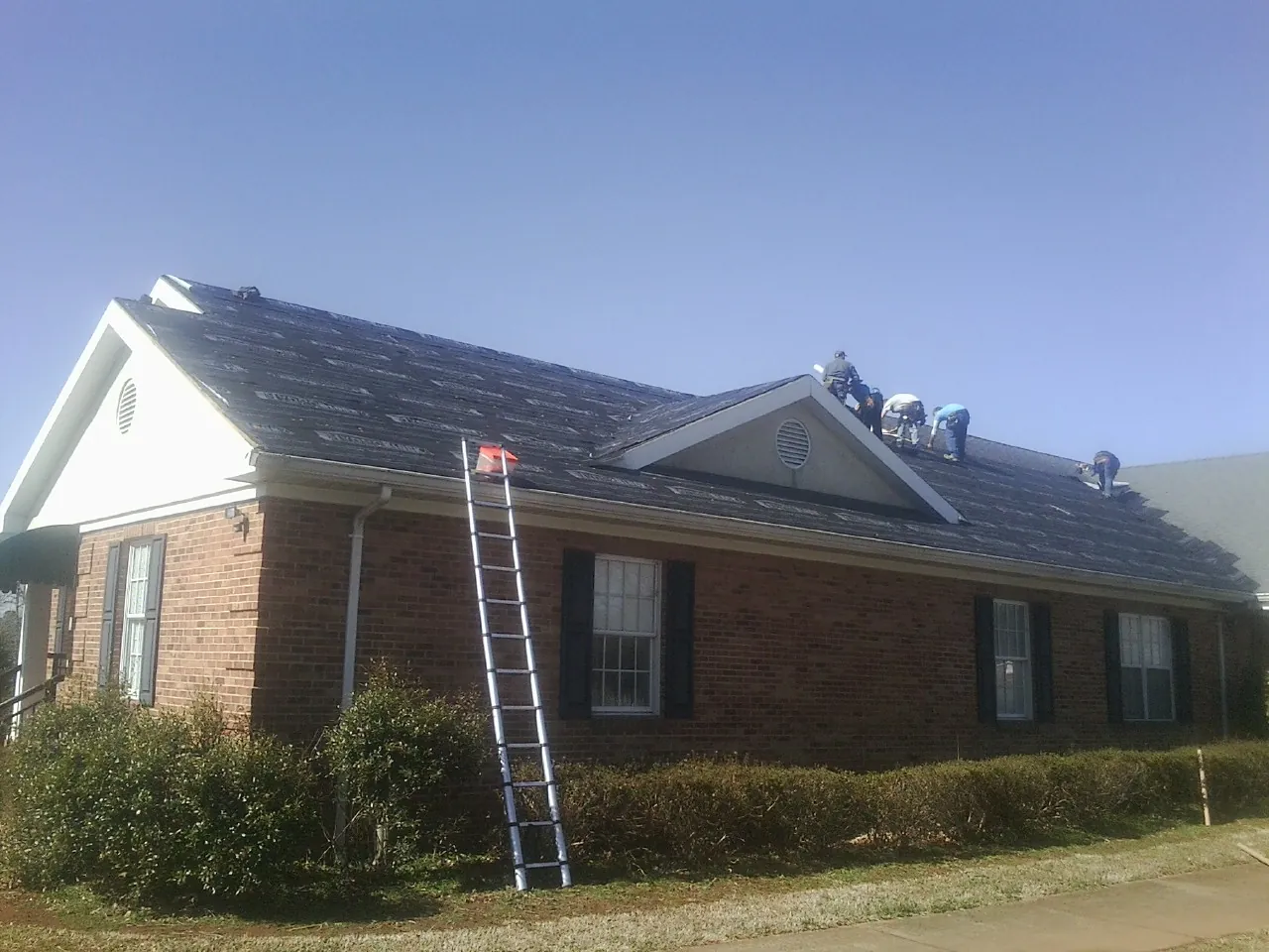 Crew tearing shingles off a brick ranch roof with a ladder set — Emergency Roof Repair work by our crew in Beverly Hills